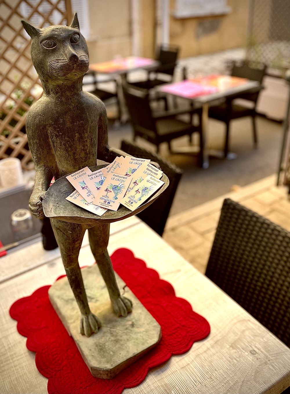Une statuette de chat debout portant un plateau de tickets, sur une table de la terrasse